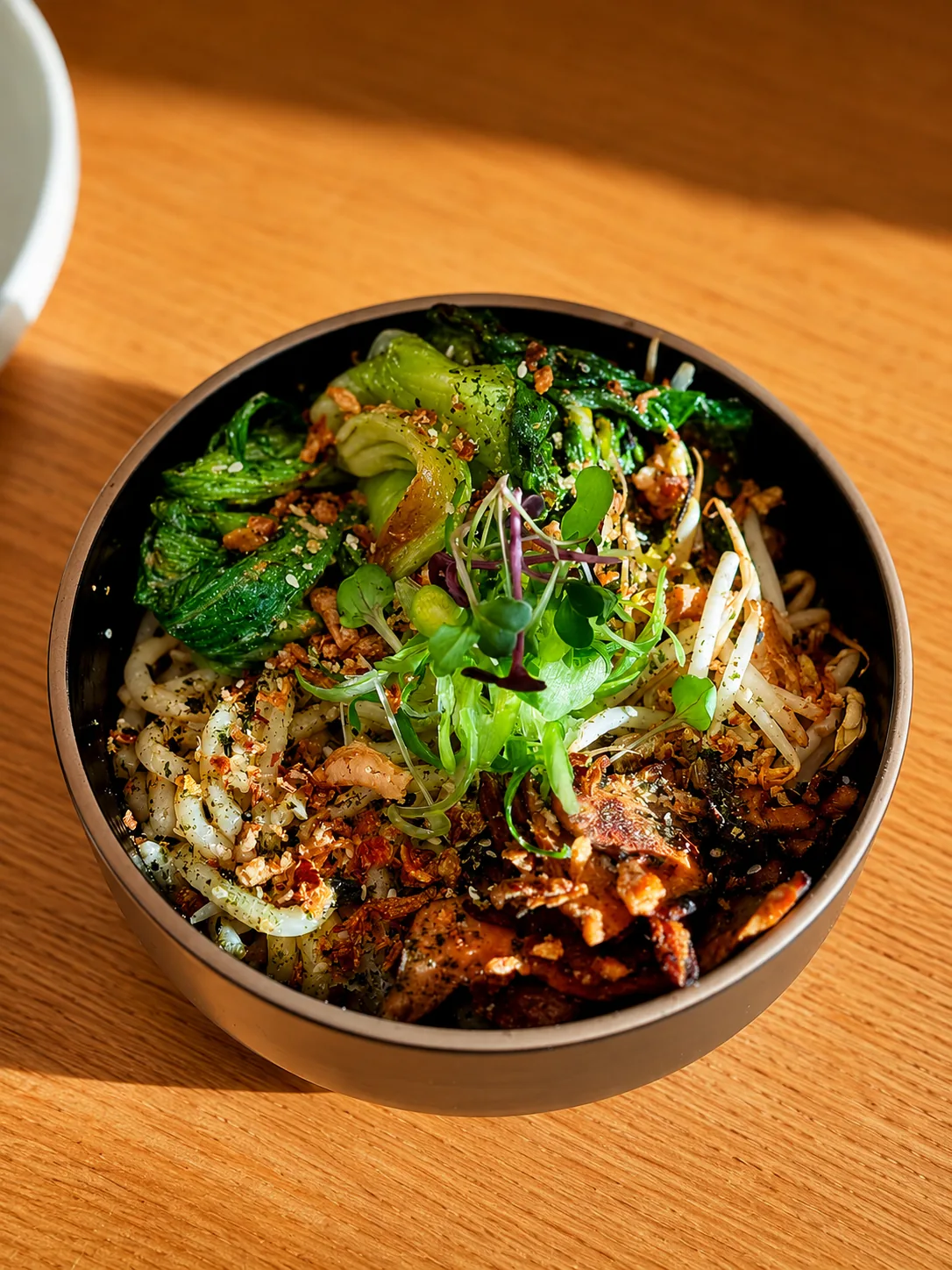 A colourful noodle lunch bowl on a timber table at Akin Cafe